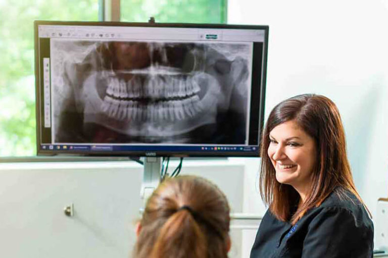 A dental assistant speaks to a patient with digital x-rays on a screen behind her
