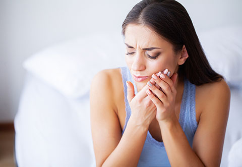 woman with toothache holding her cheek in pain