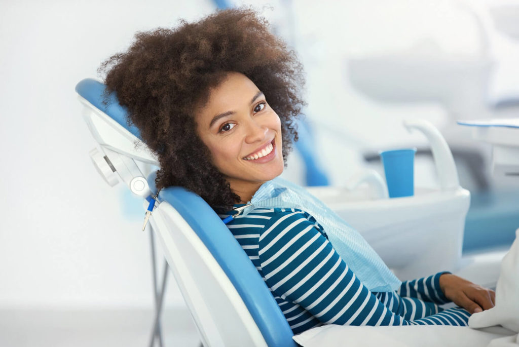 A female dental patient sits in an exam chair and looks over her shoulder smiling