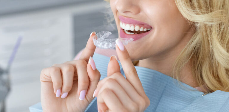smiling female patient holding a clear aligner in front of her mouth